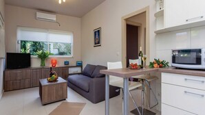 A modern kitchen with white cabinets, a microwave, and a dining area with a table and chairs. - Apartments Ankora (Dubrovnik)