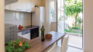 A modern kitchen with white cabinets, a built-in oven, and a dining area with a table and chairs. - Apartments Ankora (Dubrovnik)