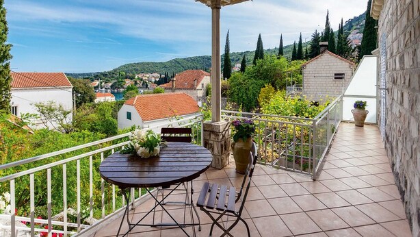 A covered outdoor area with a table and chairs, overlooking a town with red-roofed buildings and greenery. - Apartments Ankora (Dubrovnik)