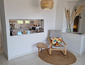 Una cocina moderna con una isla integrada, un comedor con una silla y alfombra, y un jarrón decorativo con plumas de pampa.