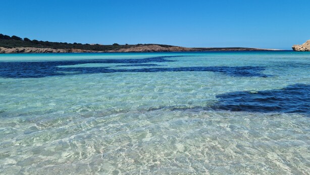 A clear coastal view with calm waters and rocky terrain.