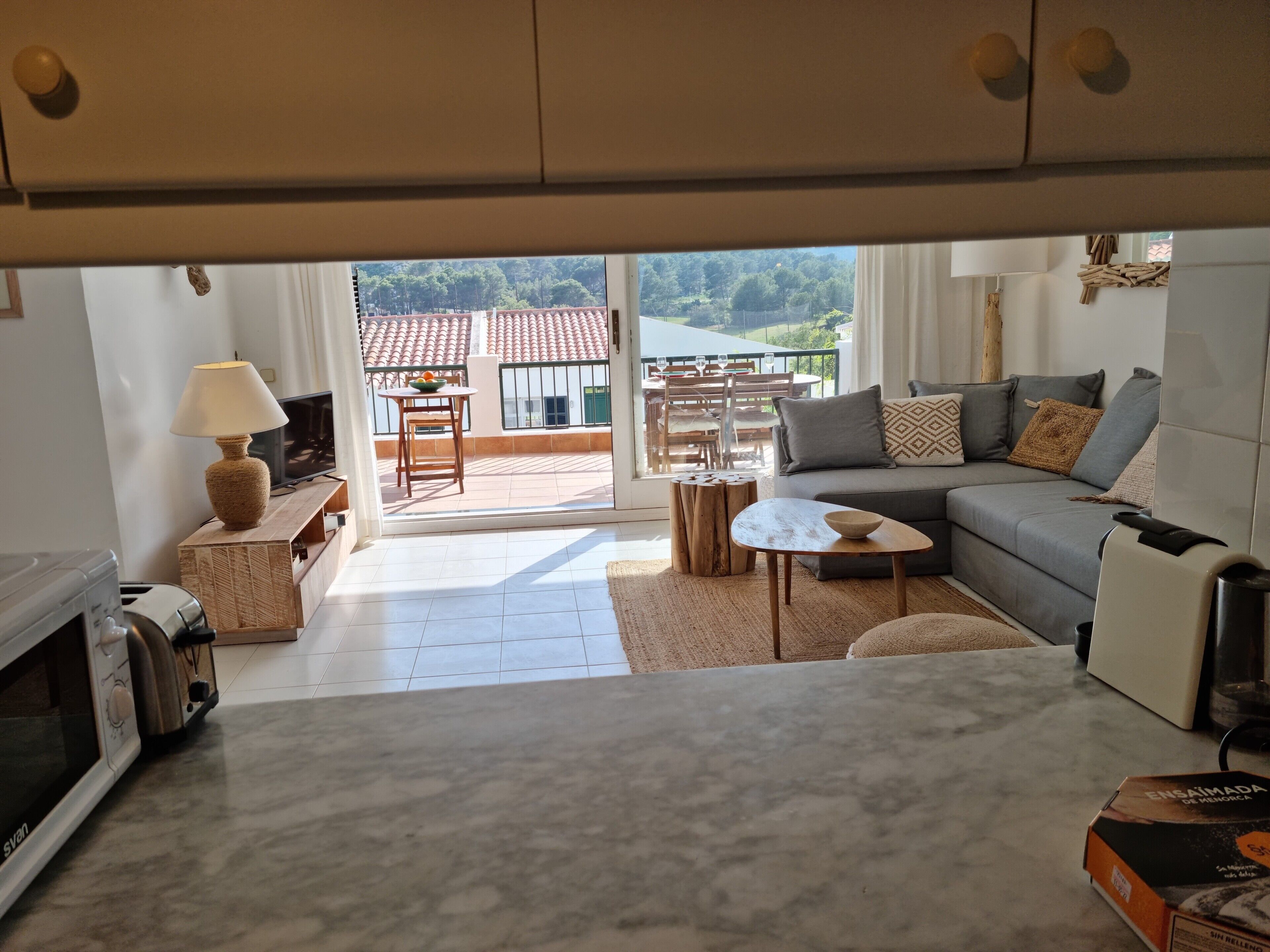 Un salon comprenant un canapé, une table, une lampe et donnant sur un balcon avec un coin repas.