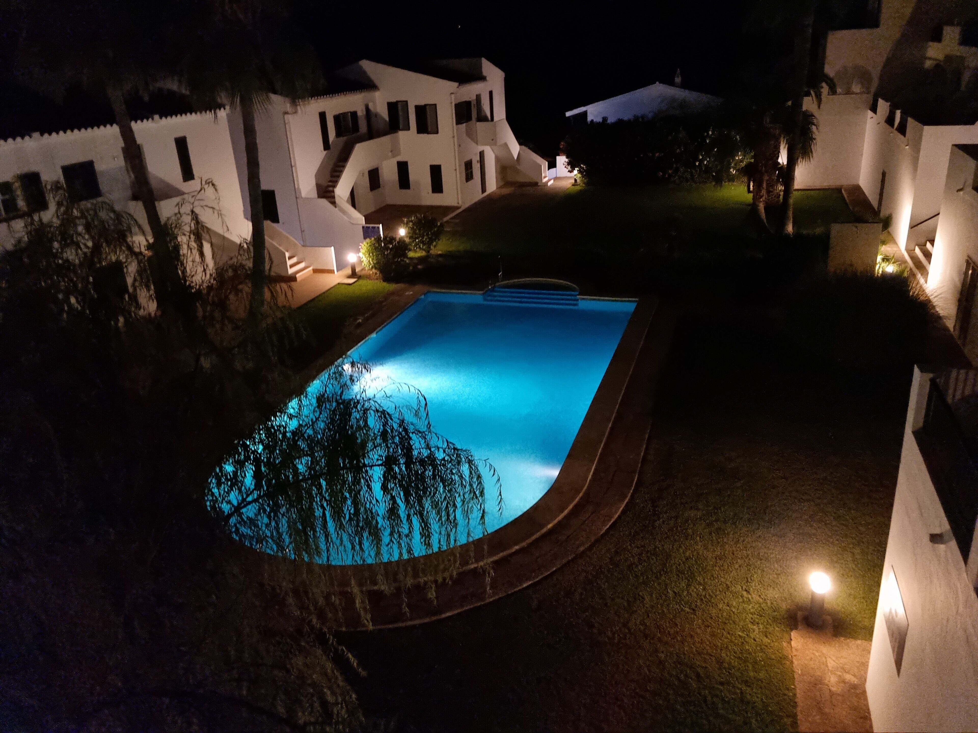 Ein Schwimmbecken, umgeben von weißen Gebäuden bei Nacht.