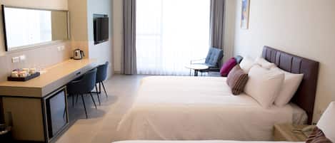 Habitación de hotel con dos camas, un escritorio con sillas, televisión y vistas al exterior.