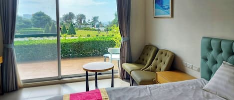 Habitación de hotel con un ventanal grande, una cama, dos sillas, una mesita y un cuadro en la pared.