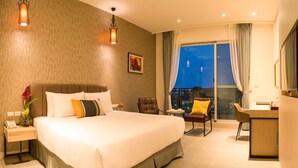 Habitación de hotel con una cama grande, un escritorio, una silla y vistas a la ciudad de noche.