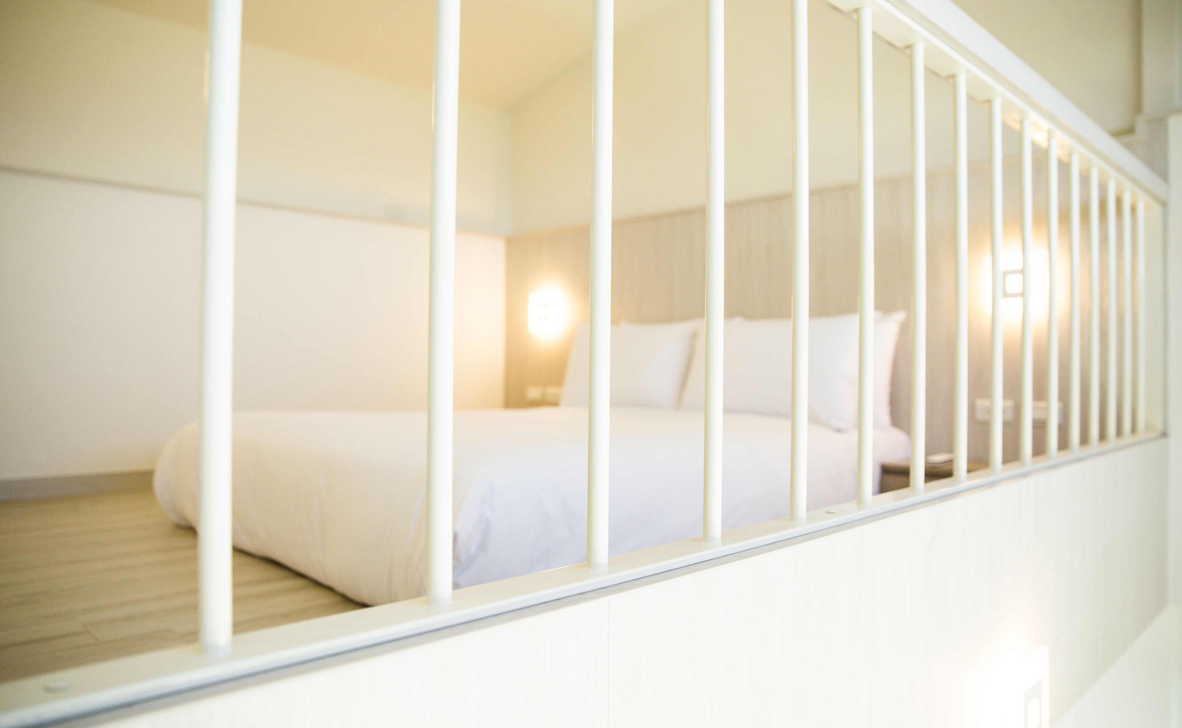 A bedroom with a bed, white walls, and a wooden floor.