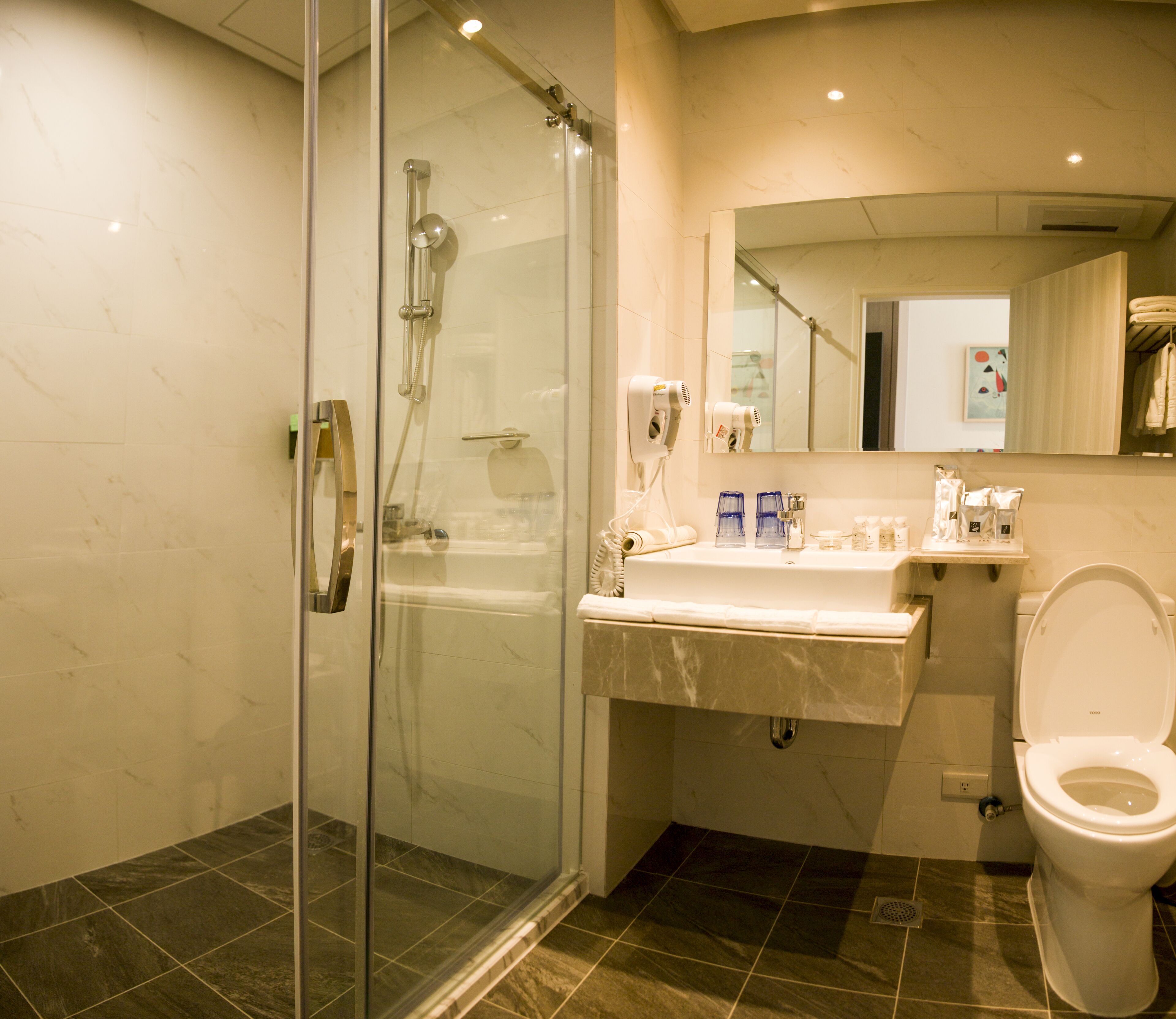 Ein modernes Badezimmer mit einer Duschkabine, Marmorboden, einem weißen Waschbecken und Toilettenartikeln sowie einer Toilette.