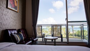 Habitación de hotel con una cama grande, un sofá de cuero, una pequeña mesa redonda y un balcón con vista al océano y palmeras.