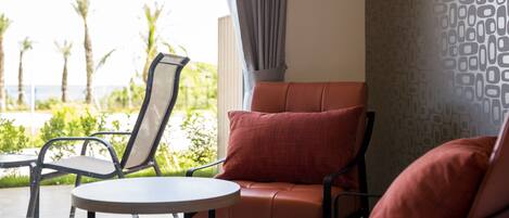 A room with a view of palm trees and a pool, a round table, and a red cushioned chair.