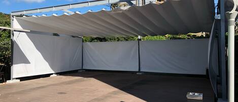 Un espacio de patio al aire libre con toldo blanco, piso de ladrillo y baranda metálica.