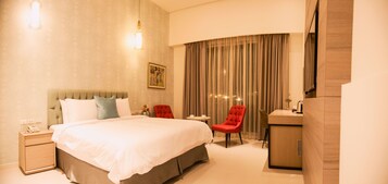 A hotel room with a large bed, a red chair, a small table, and a desk with a mirror.