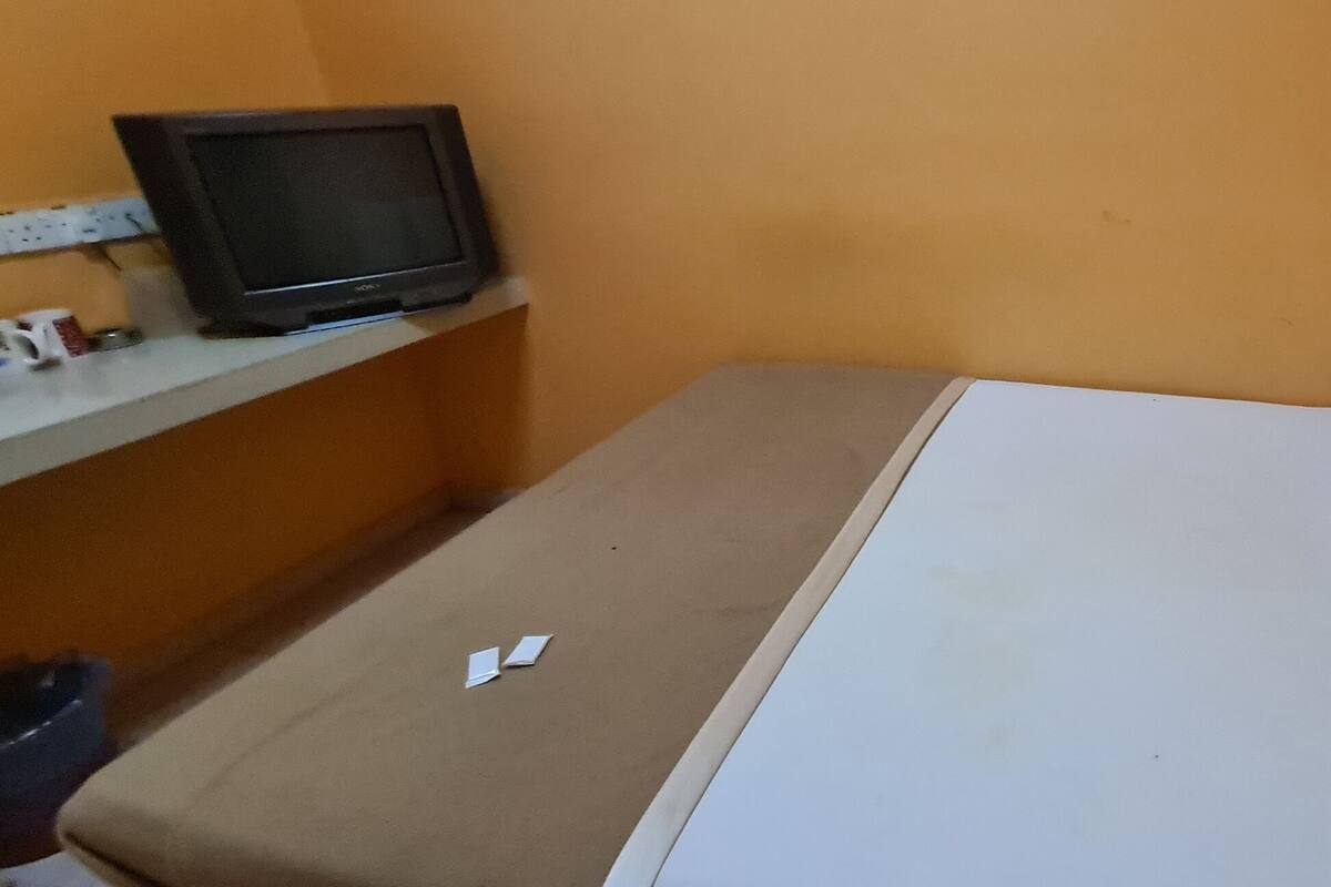 A small, single-bed room with a television on a shelf, a white pillow, and a beige mattress.
