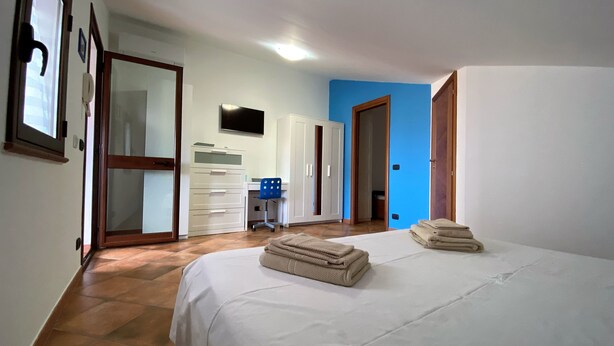 A bedroom with a bed, a desk, a chair, a wardrobe, and a television on the wall. - BlueMoon Home (Campofelice di Roccella)