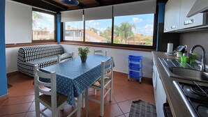 A compact kitchen with a dining area, a window with a view of the neighborhood, and a ceiling fan. - BlueMoon Home (Campofelice di Roccella)