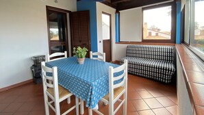 A dining area with a table covered in a blue checkered tablecloth, two white chairs, a patterned sofa, and a potted plant. - BlueMoon Home (Campofelice di Roccella)