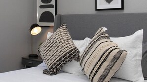 Un letto rifatto con due cuscini decorati, una lampada da comodino e un quadro appeso alla parete.