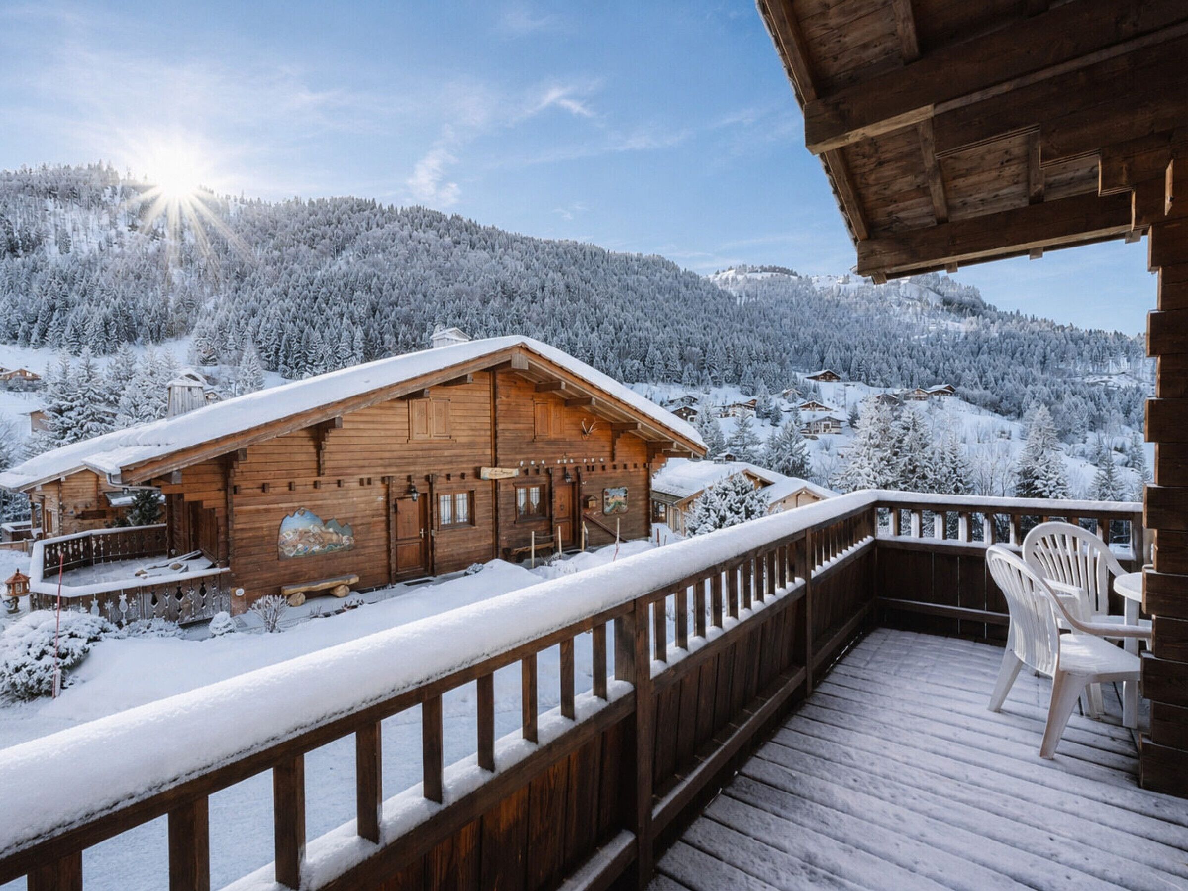 A wooden cabin with a balcony, surrounded by snow-covered trees and a mountainous backdrop.