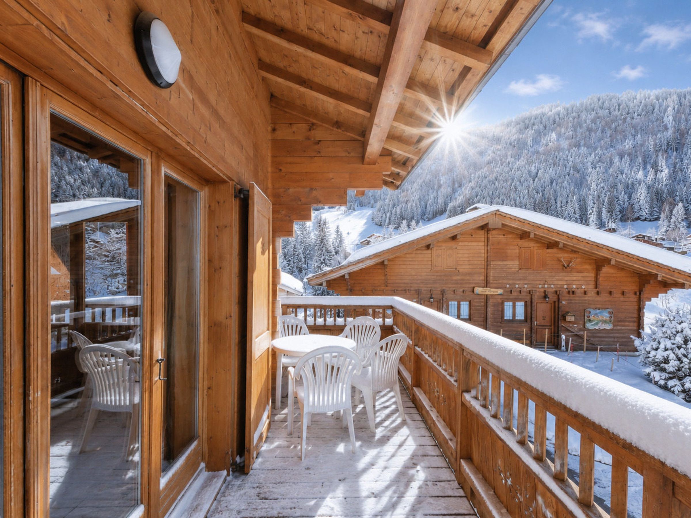 Une cabane en bois avec un balcon, des chaises blanches et une vue sur une montagne enneigée.