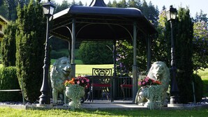 Um gazebo com duas estátuas de leão, cercado por vegetação e um caminho.