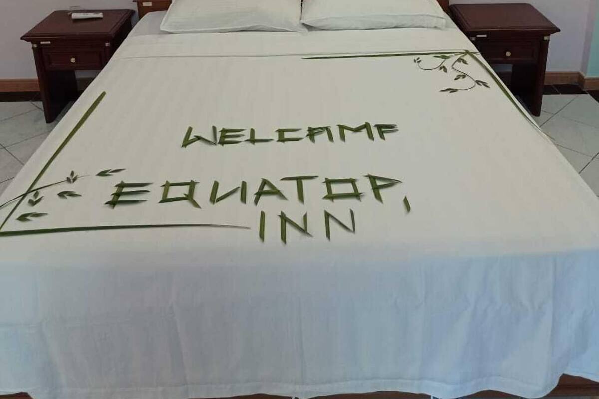 A bed with a white bedspread featuring the text "Welcome Equator Inn."