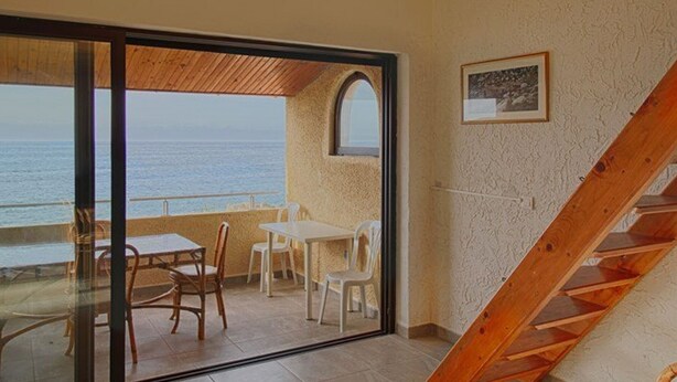 A room with a glass door leading to a balcony with a view of the sea. There is a wooden staircase inside the room. - Nice 2-room Apt, 4 people, Lumio, AC, parking (Lumio)