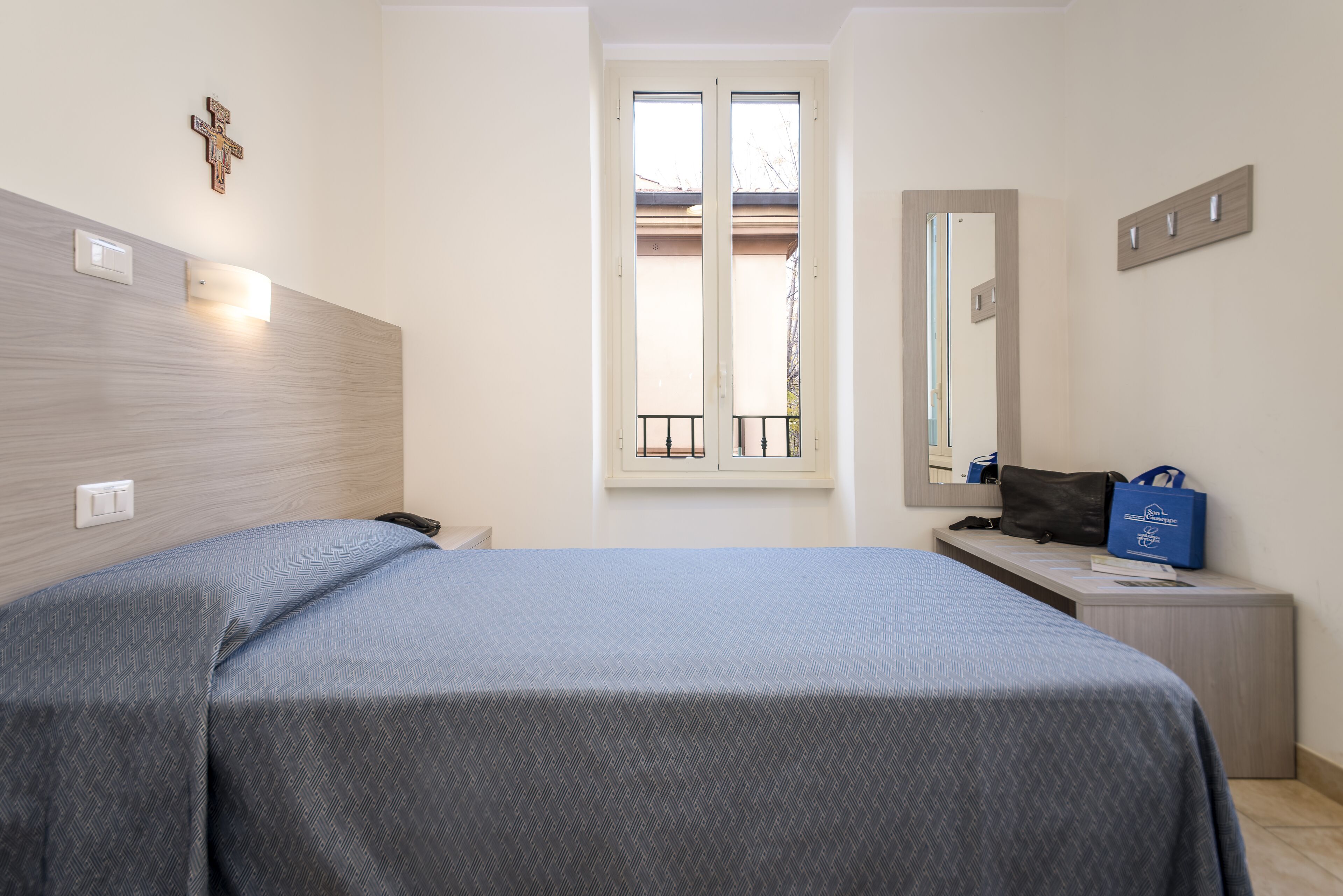 Un dormitorio con cama, mesita de noche, espejo y ventana.