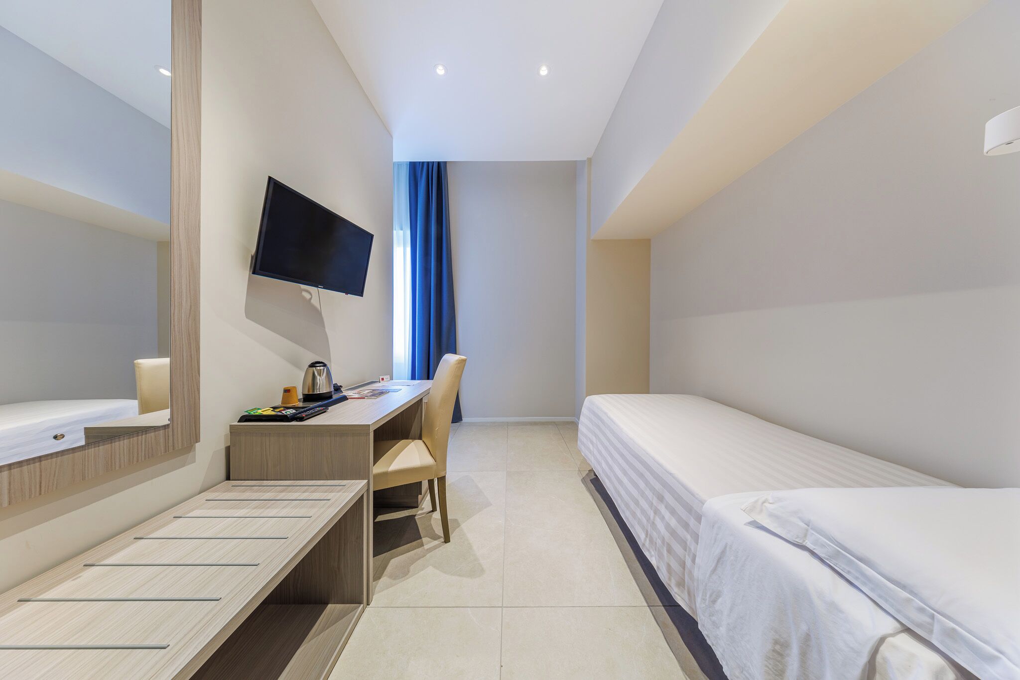Habitación de hotel con cama, escritorio, silla, televisor montado en la pared y ventana con cortinas.
