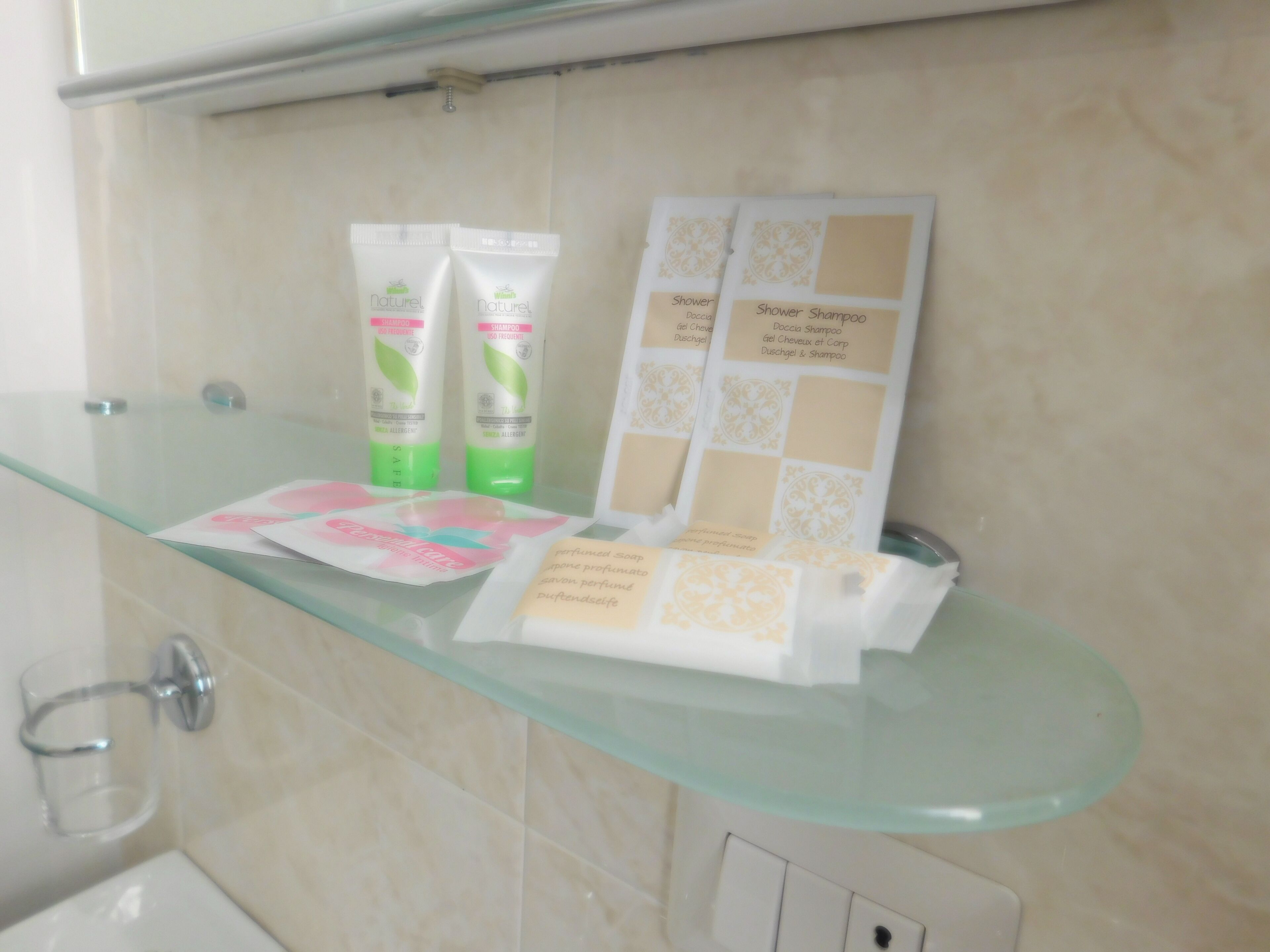 Ein Badezimmer mit einer Glasablage, auf der Toilettenartikel, darunter Shampoo und Duschgel, liegen.