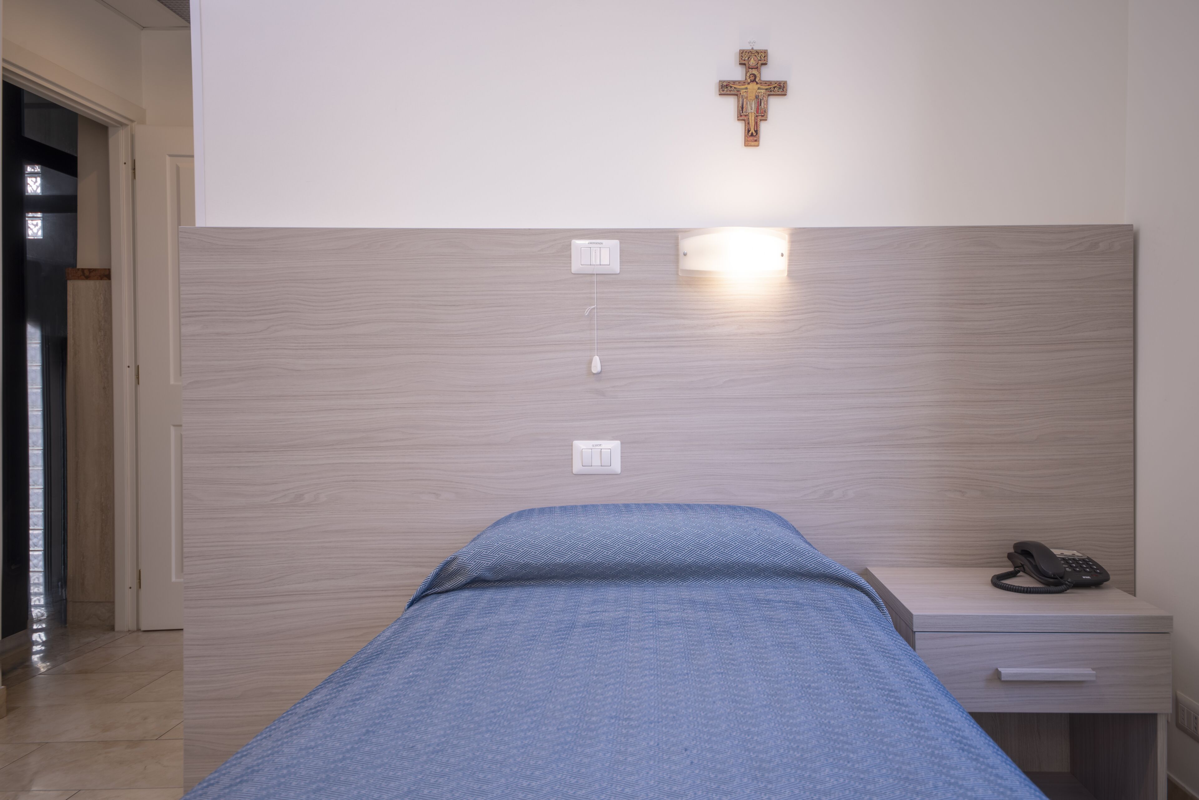 Un dormitorio con cama, mesita de noche y una cruz colgada en la pared.