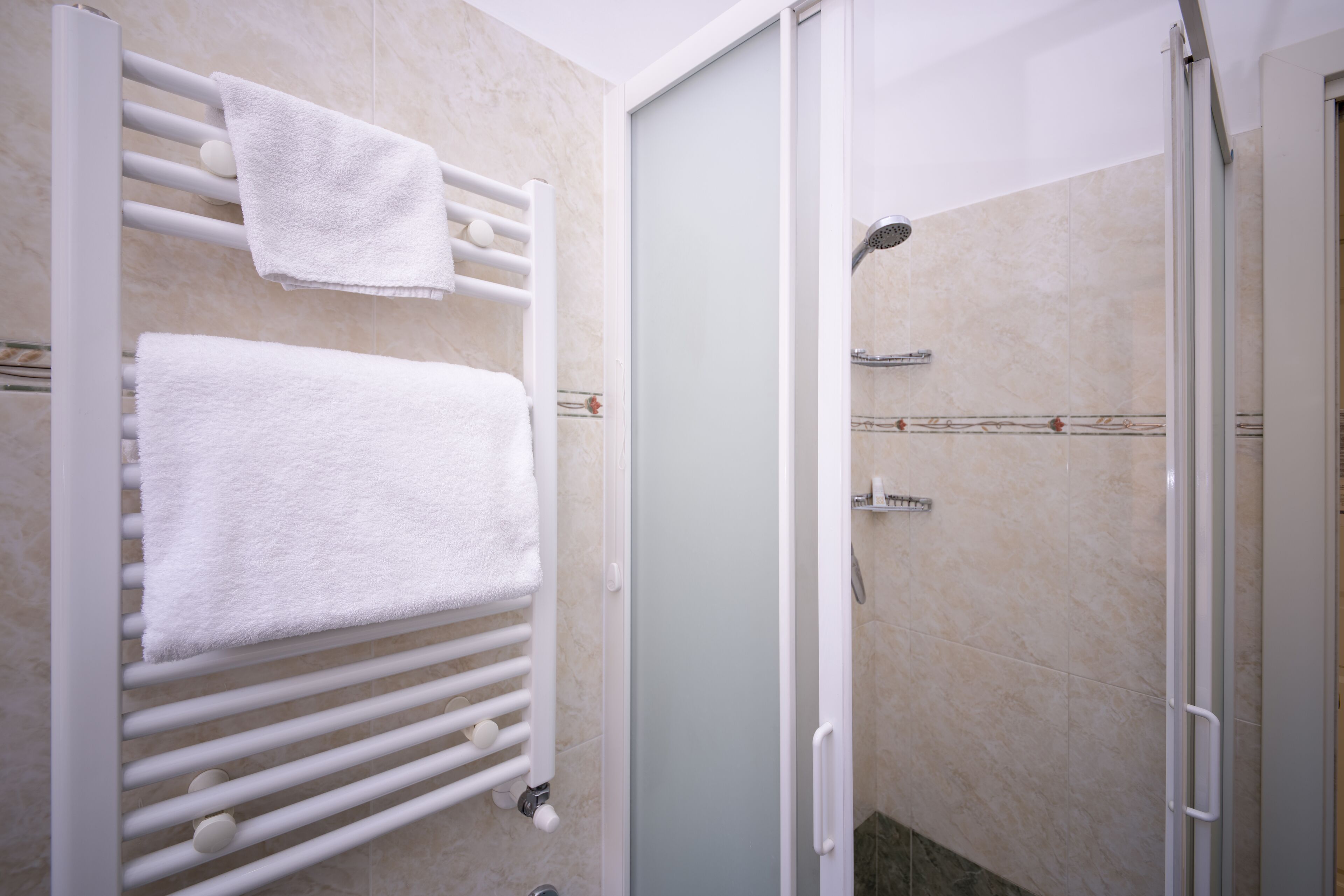A bathroom with a white towel rack, a glass shower enclosure, and beige tiled walls.