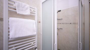 A bathroom with a white towel rack, a glass shower enclosure, and beige tiled walls.