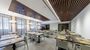 A modern dining area with multiple tables and chairs, a bar area, and large windows allowing natural light. - Casa San Giuseppe (Rome)