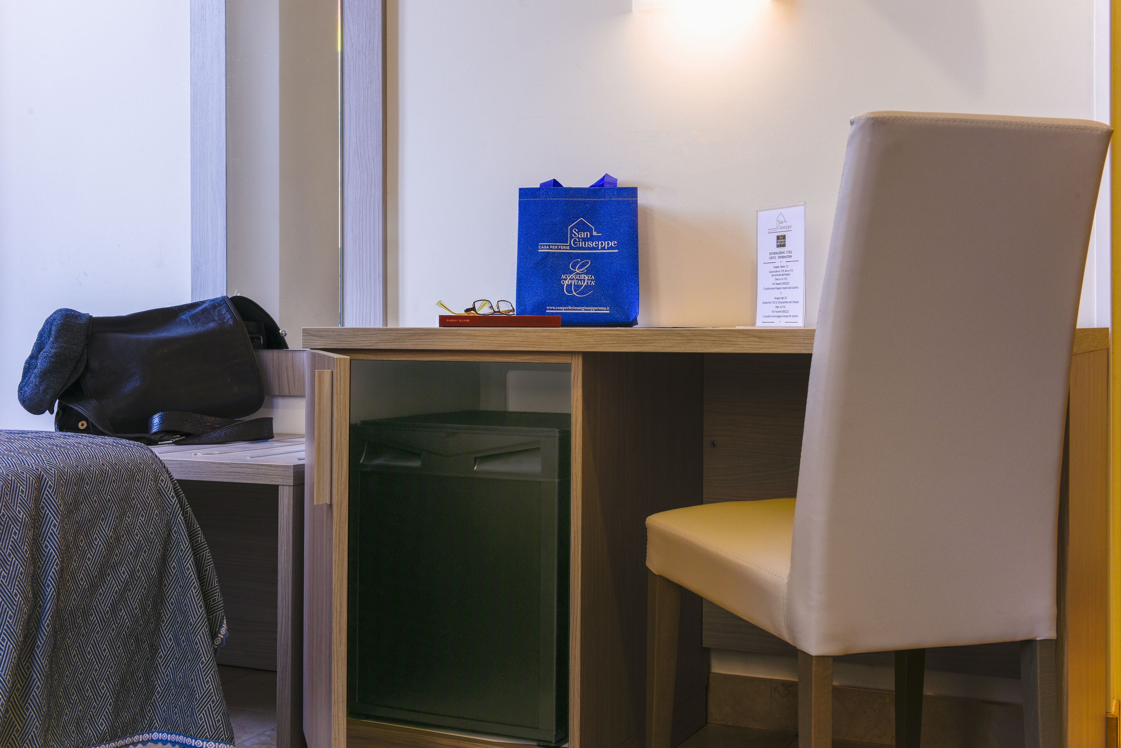 Ein Hotelzimmer mit Schreibtisch, Stuhl, Mülleimer und blauer Tasche auf dem Schreibtisch.