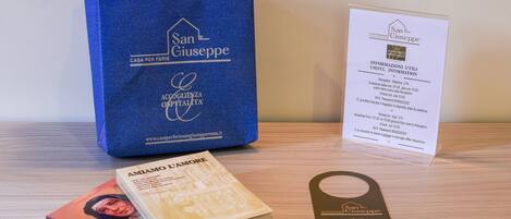 A blue bag with "San Giuseppe" branding, a booklet, a book titled "AMIAMO L'AMORE", and a hotel information card.