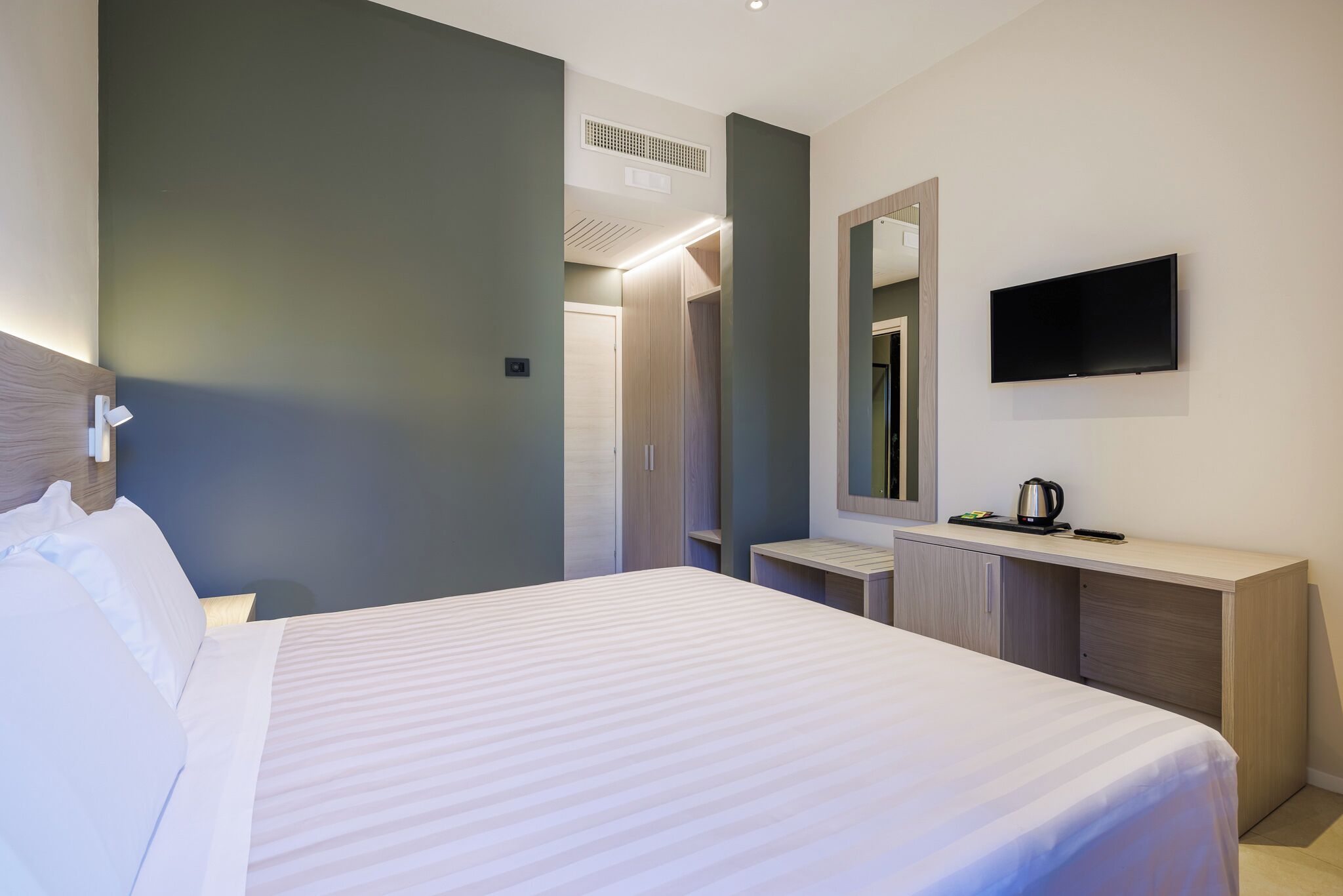 Una habitación de hotel con una cama, una mesita de noche, un espejo, un televisor y un armario.