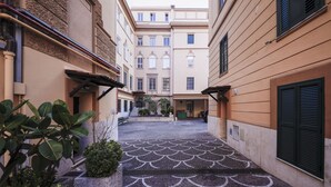 A narrow alleyway with a tiled floor featuring a scalloped pattern, flanked by buildings with balconies and shutters. - Casa San Giuseppe (Rome)
