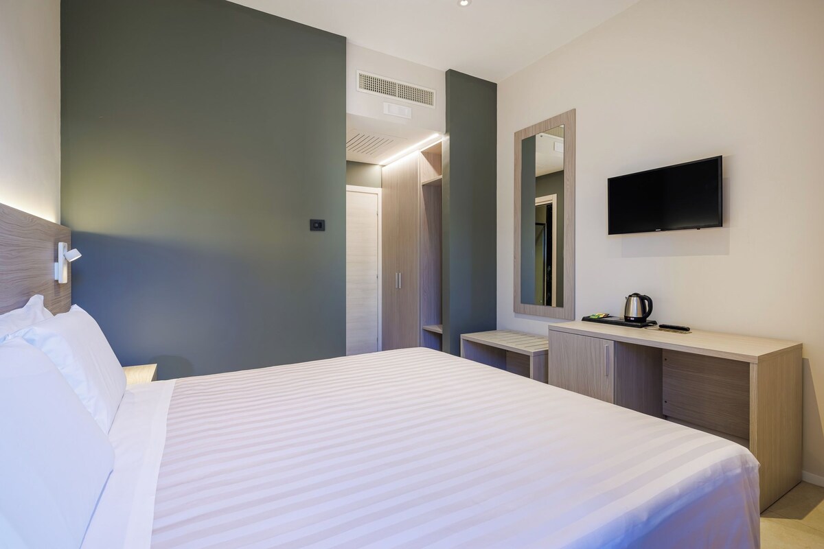 A hotel room with a bed, a bedside table, a mirror, a TV, and a wardrobe.