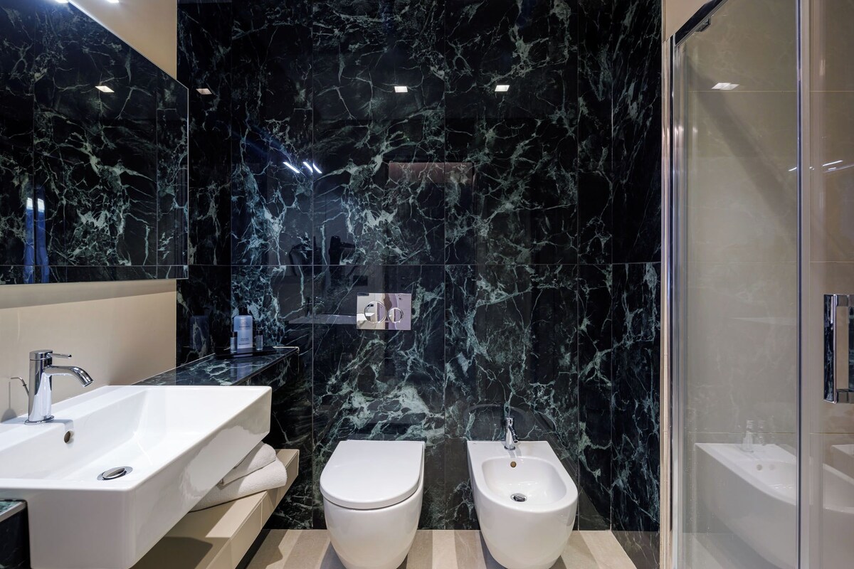 A modern bathroom with a large mirror, two sinks, a bidet, and a shower.