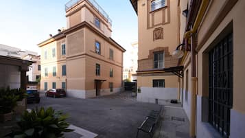 A courtyard with a bench, a car, and a building with a balcony.