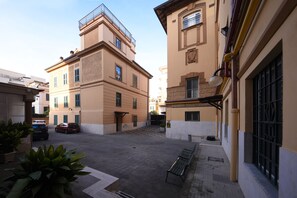 Un patio con un banco, un coche y un edificio con balcón.