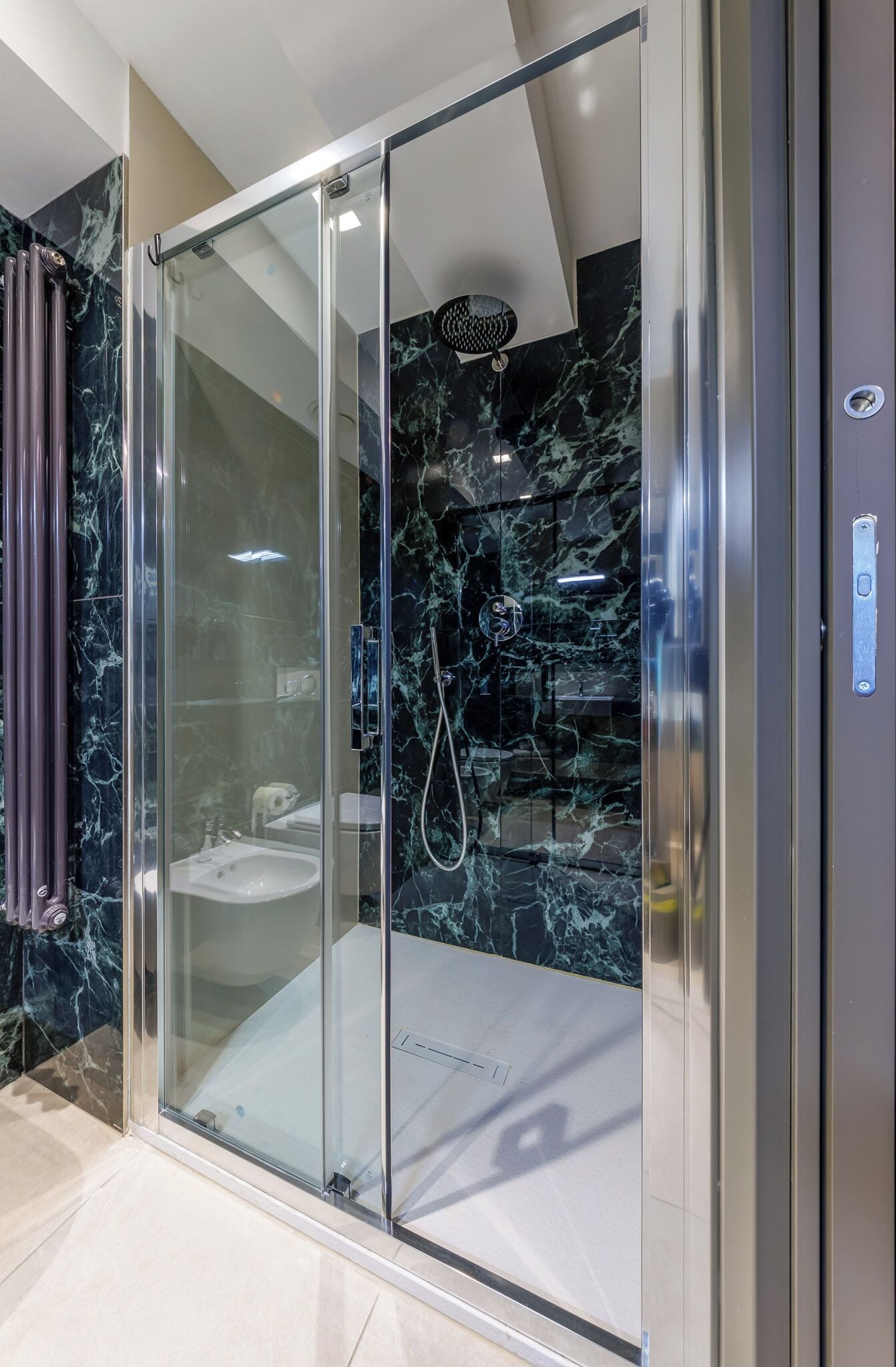 Un baño moderno con cabina de ducha de vidrio, paredes de mármol y un inodoro a la vista.