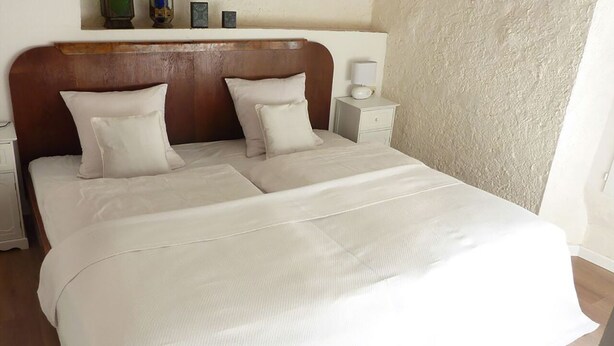 Een net opgemaakt bed met een houten hoofdbord, twee nachtkastjes met lampen, en een gestructureerde muur.