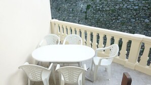 Een balkon met een witte tafel en stoelen, een stenen muur en een witte balustrade.