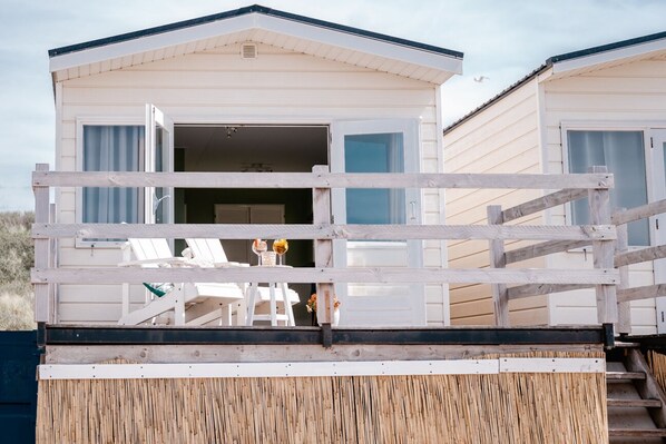 A white mobile home with an open door, a wooden deck, and a small outdoor seating area with a table and chairs.