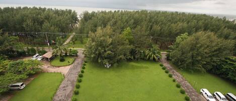 Vista aerea di una proprietà con un ampio prato verde, un’area di parcheggio con diverse auto e una fitta foresta sullo sfondo.