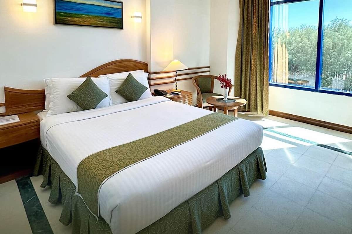 A hotel room with a large bed, a nightstand, a chair, a small table, and a window with a view.