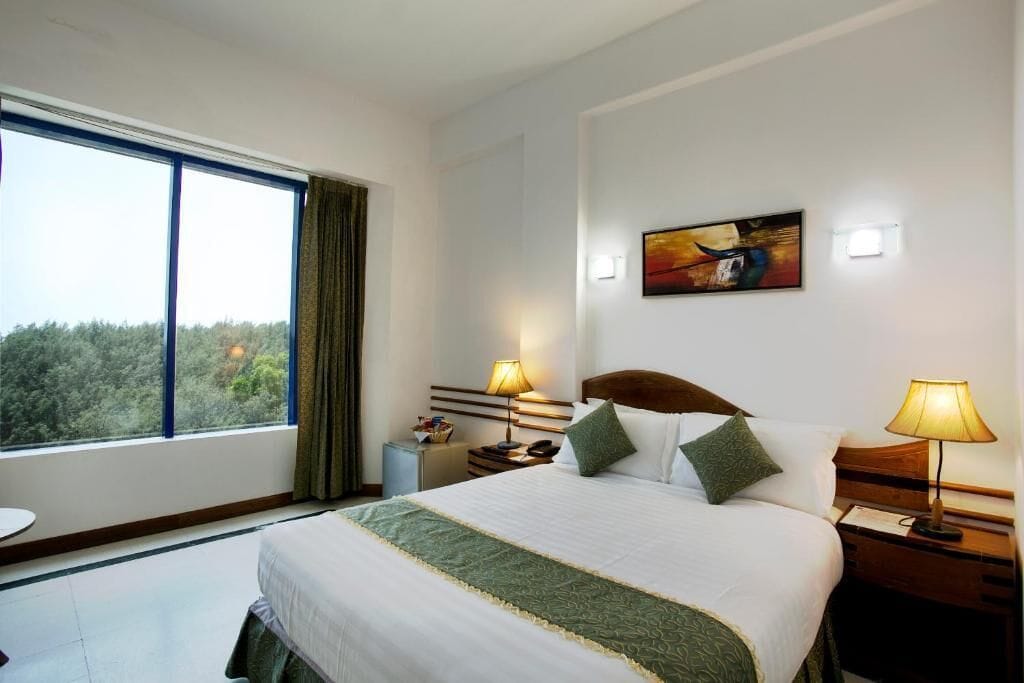 Habitación de hotel con una cama grande, dos mesitas de noche con lámparas, un cuadro en la pared y vistas del bosque por la ventana.