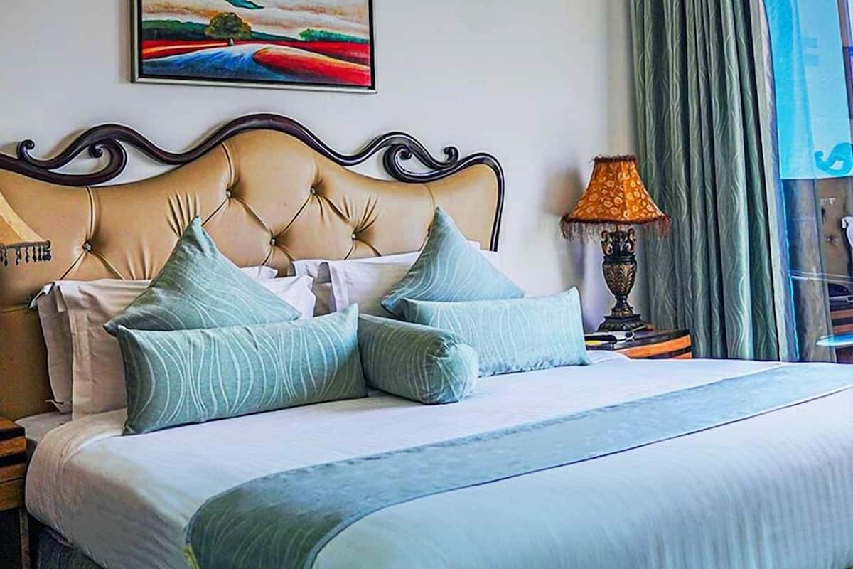 A neatly made bed with a tufted headboard, a bedside lamp, and a painting on the wall.