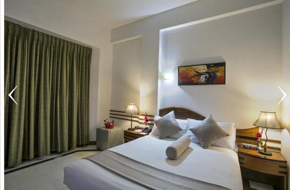 A hotel room with a large bed, two bedside tables, a painting on the wall, and a green curtain.
